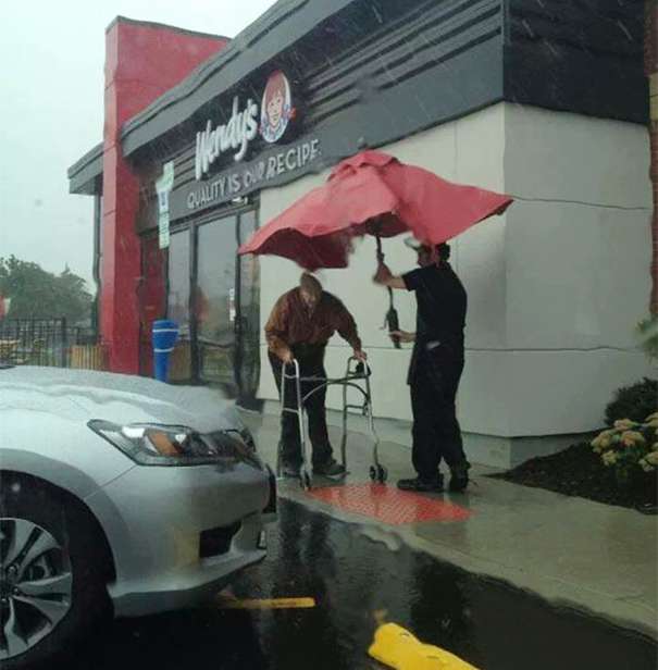 Wendy’s employee holding umbrella to protect an old man from the rain